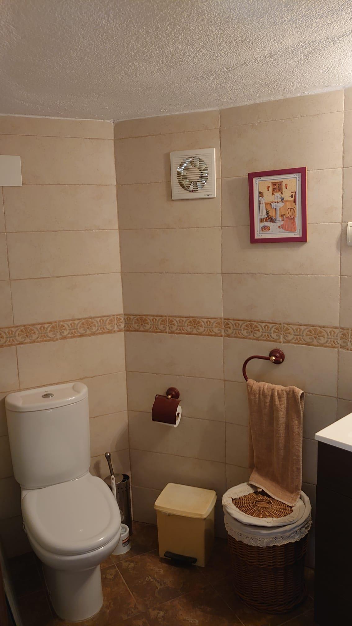 Salle d'eau fonctionnelle avec carrelage crème, frise ornementale et sanitaires blancs. Comprend des accessoires en bois sombre et un panier en osier.