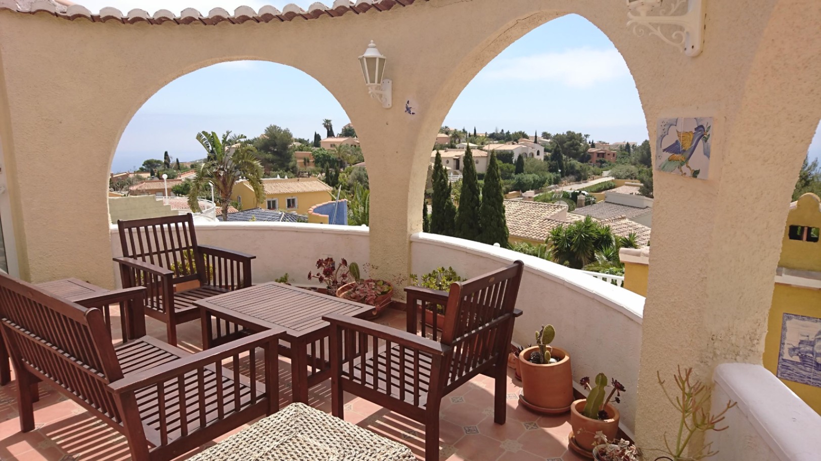 Terrasse couverte avec arches en ogive, mobilier en bois sombre et sol en terre cuite. Elle offre une vue dégagée sur le quartier et la mer.