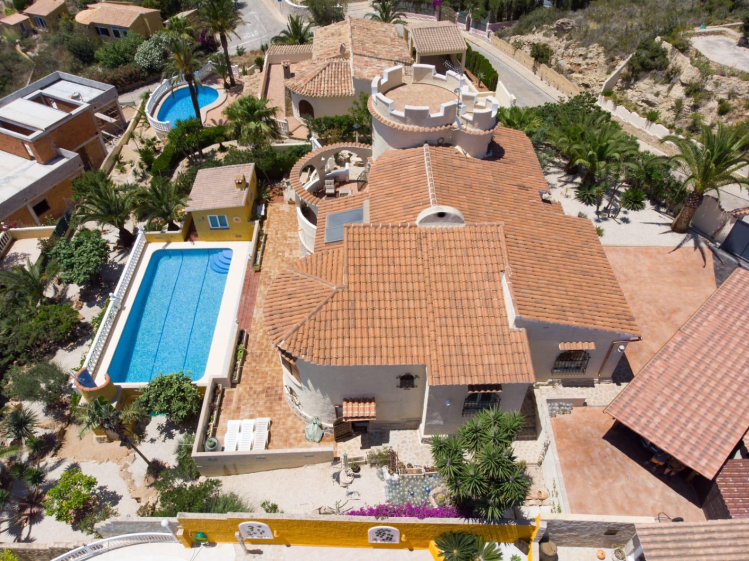 Vue aérienne de la villa avec toiture en tuiles, tour blanche caractéristique, piscine rectangulaire de 10x4m et jardin méditerranéen arboré de palmiers.