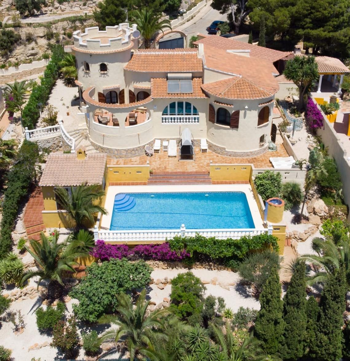 Vue aérienne de la villa méditerranéenne avec sa tour ronde, une piscine de 10x4m entourée d'une balustrade blanche et un jardin paysager avec palmiers.