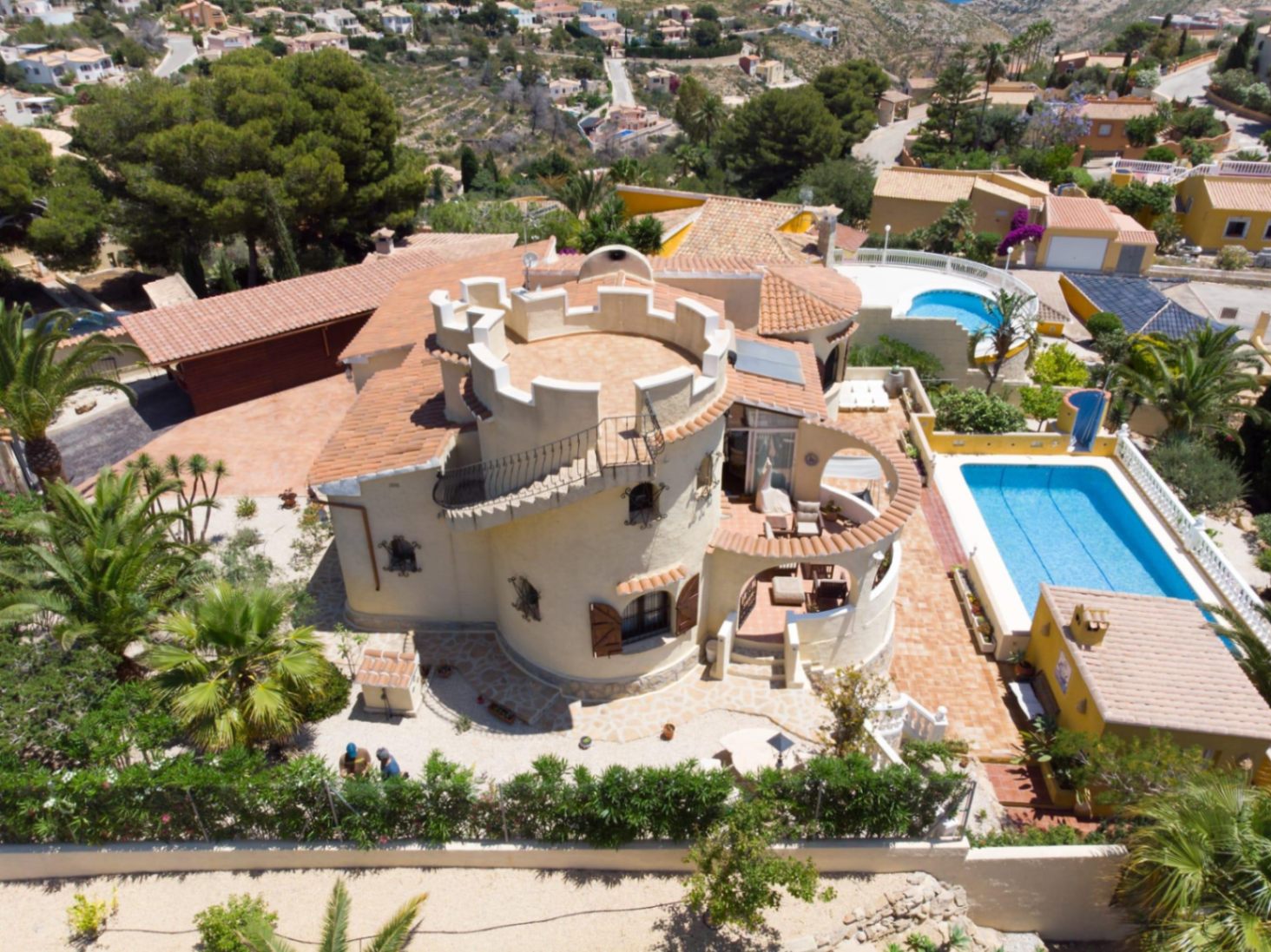 Vue aérienne de la villa montrant sa tour crénelée distinctive, sa piscine privée et ses terrasses en terre cuite au cœur d'un jardin méditerranéen.