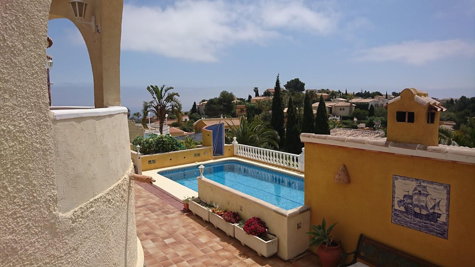 Vue surélevée de la piscine rectangulaire, terrasse en terre cuite, murs ocres ornés de céramiques et jardin méditerranéen avec horizon marin.
