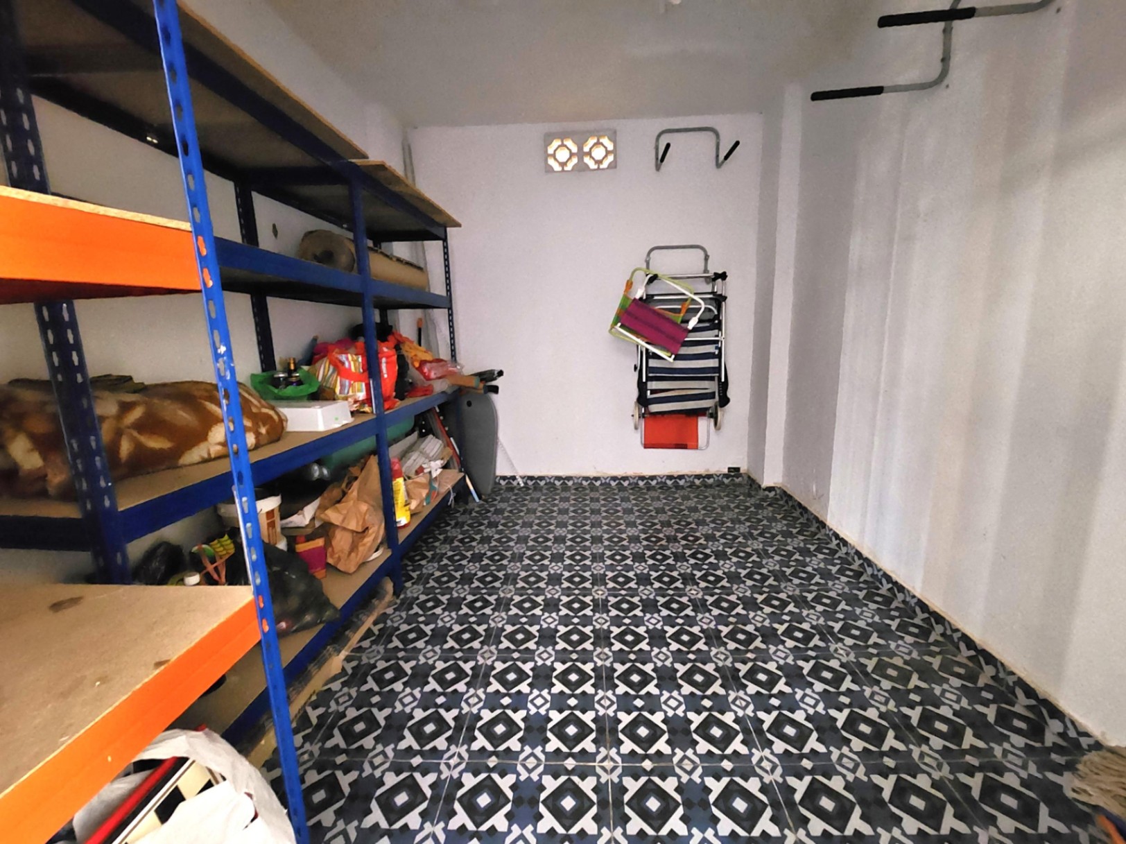 Débarras spacieux de 12 m² avec sol en carrelage à motifs géométriques, étagères métalliques robustes et murs blancs avec aération naturelle.