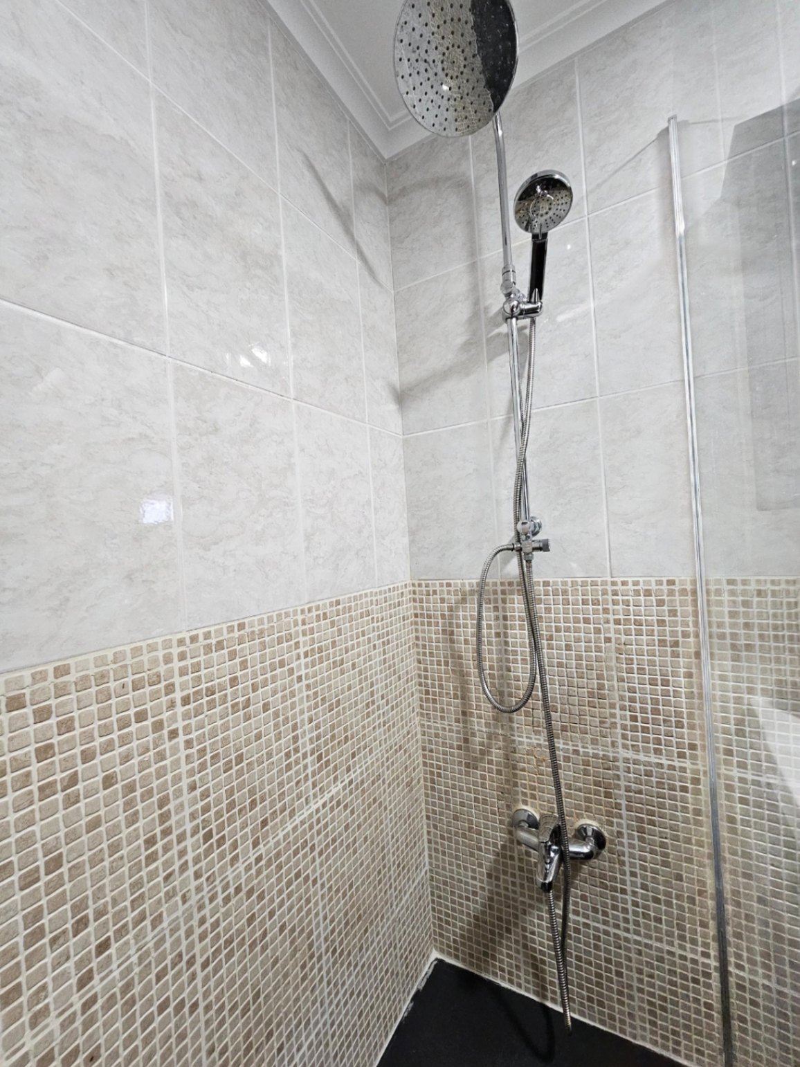 Douche contemporaine avec double pommeau, carrelage effet marbre et détails en mosaïque aux tons terreux.