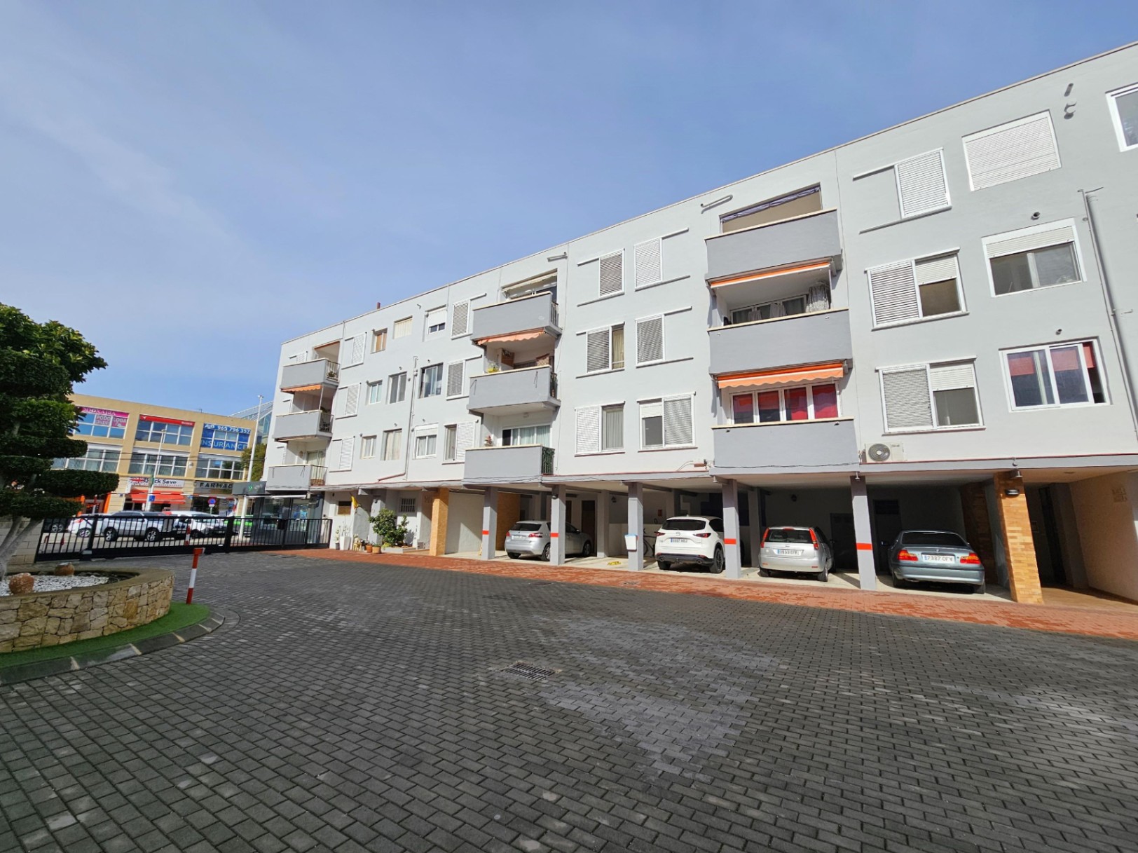 Façade extérieure de l'immeuble à Jávea, incluant des places de parking privées couvertes et des balcons avec stores bannes.