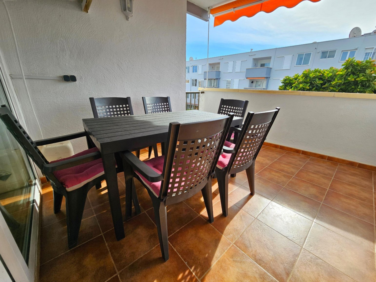 Grande terrasse avec carrelage en terre cuite, équipée d'un ensemble de repas extérieur et d'un store banne orange rétractable.