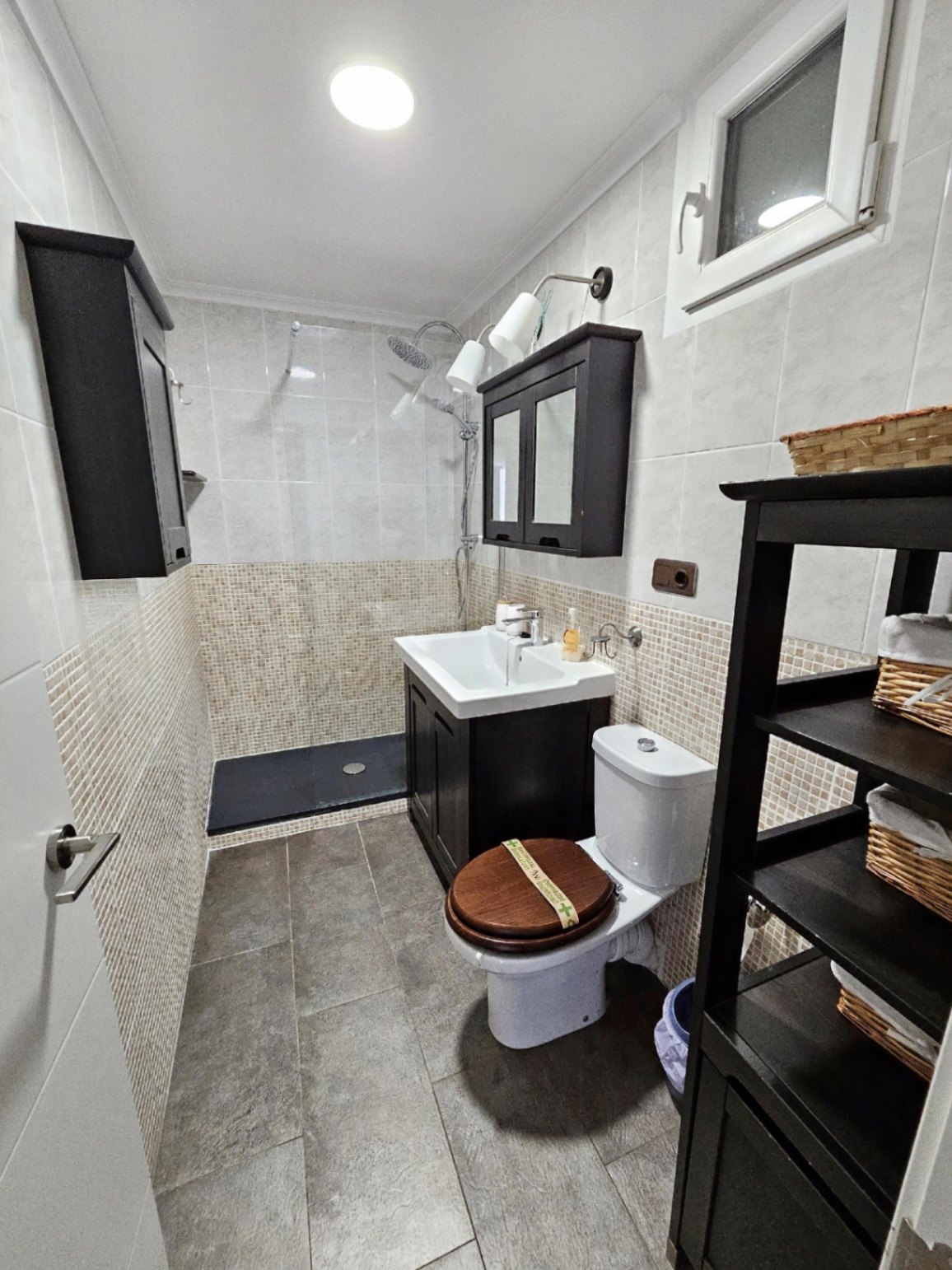 Salle de bain rénovée avec douche à l'italienne, parois en mosaïque et mobilier en bois sombre offrant un design contemporain et fonctionnel.