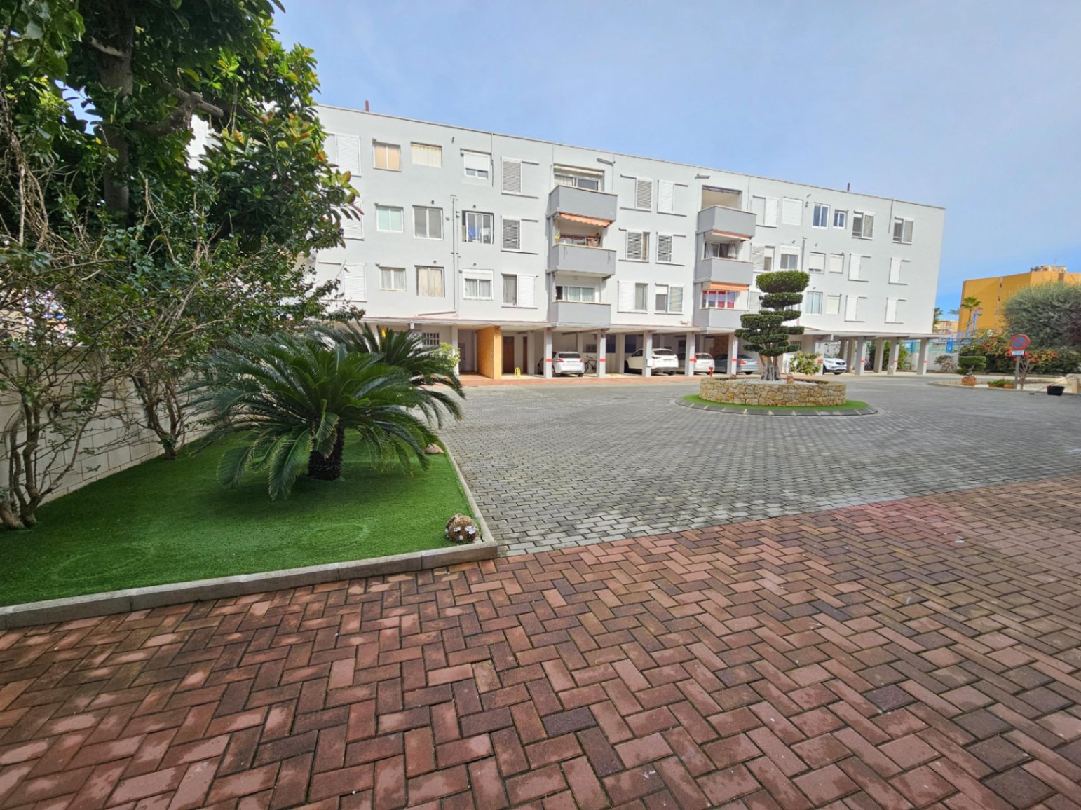 Vue extérieure du bâtiment résidentiel avec parking privé couvert, espaces verts paysagers et cour pavée dans le quartier de l'Arenal.