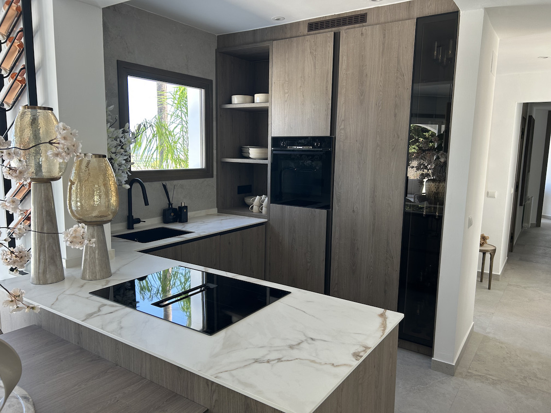 Cuisine moderne avec plans de travail effet marbre, plaque à induction intégrée et meubles en bois sombre. Comprend un évier noir mat et des appareils encastrés.