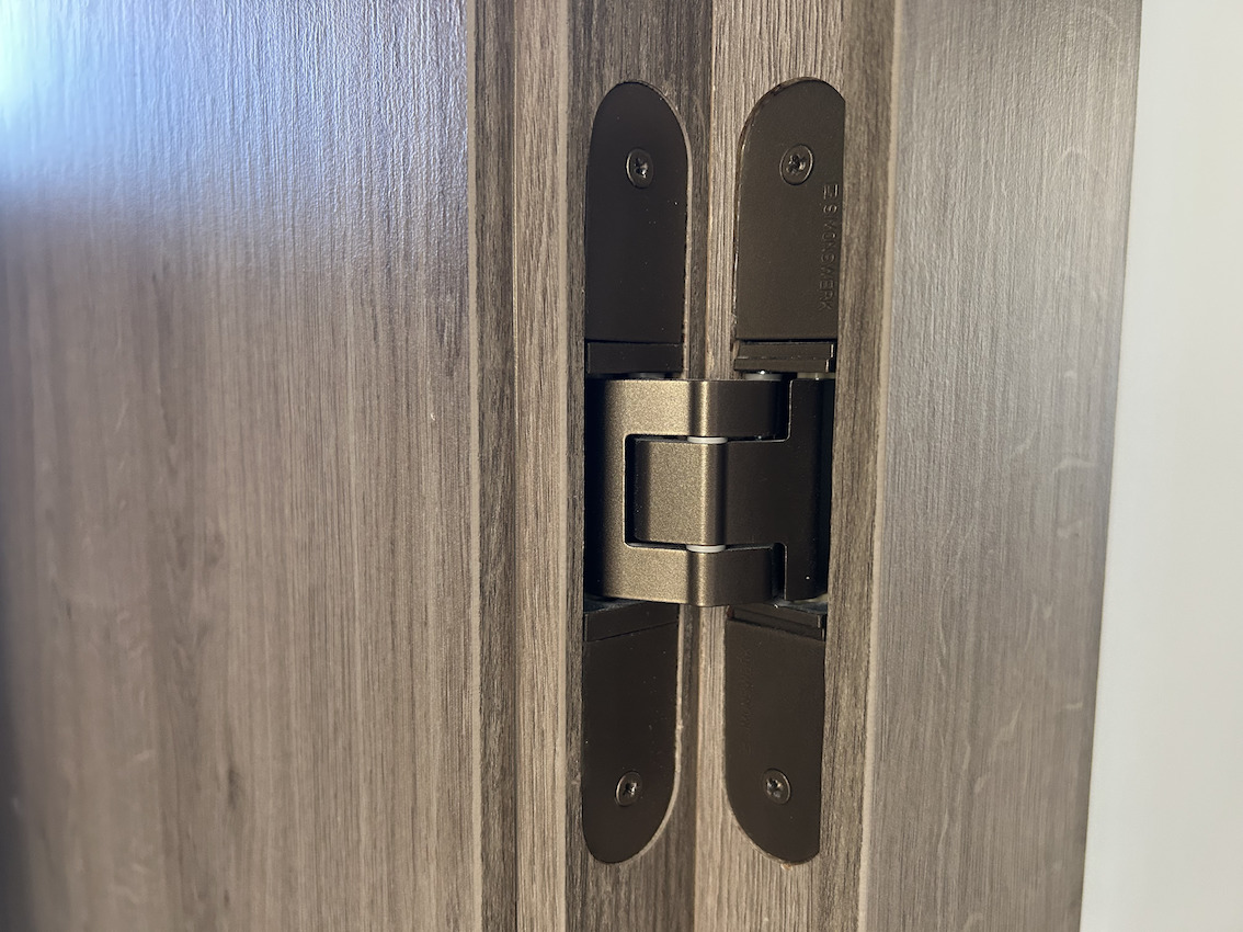 Détail d'une charnière invisible haut de gamme en finition bronze, intégrée dans une menuiserie en bois sombre pour un design épuré et moderne.