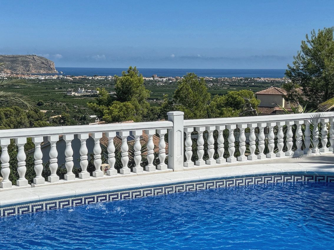 Piscine avec bordure en mosaïque bleue et balustrade blanche, offrant une vue panoramique sur la mer Méditerranée, la vallée et le littoral environnant.