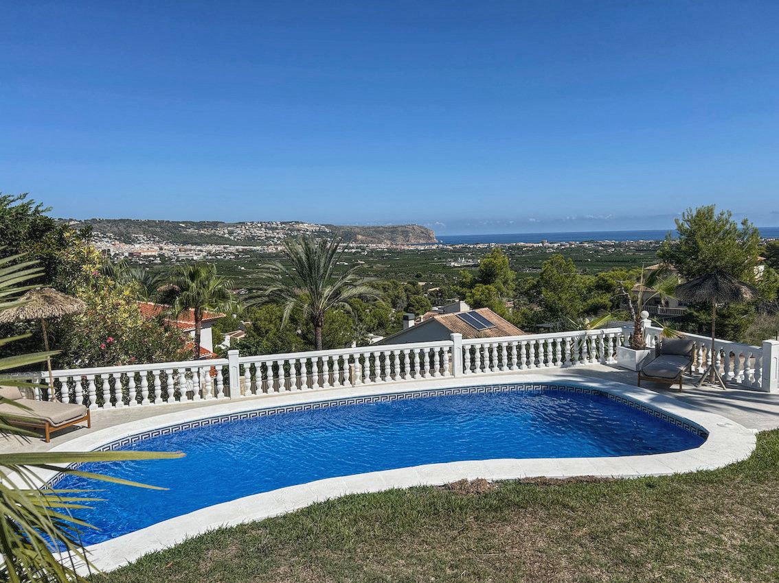 Piscine extérieure de forme incurvée avec balustrade blanche, offrant une vue panoramique sur la vallée et la mer Méditerranée.