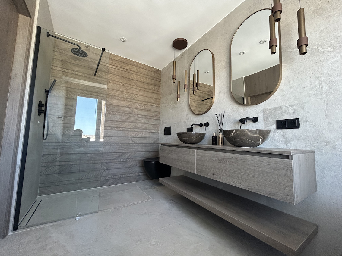 Salle de bain moderne avec double vasque en pierre, robinetterie noire encastrée et douche à l'italienne avec mur d'accent aspect bois.