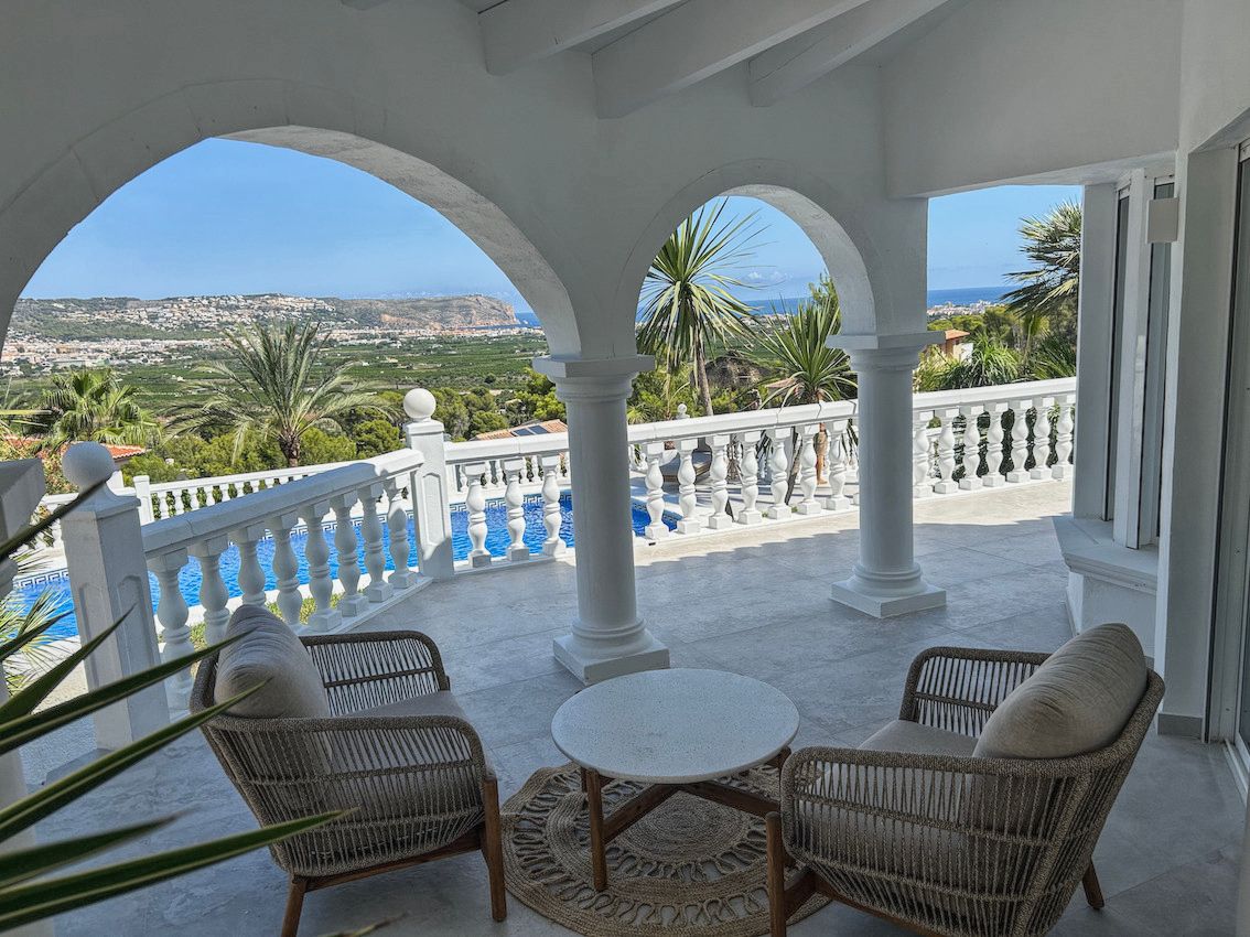 Terrasse couverte avec arches blanches, mobilier en rotin et vue panoramique sur la piscine, la vallée et la mer Méditerranée.