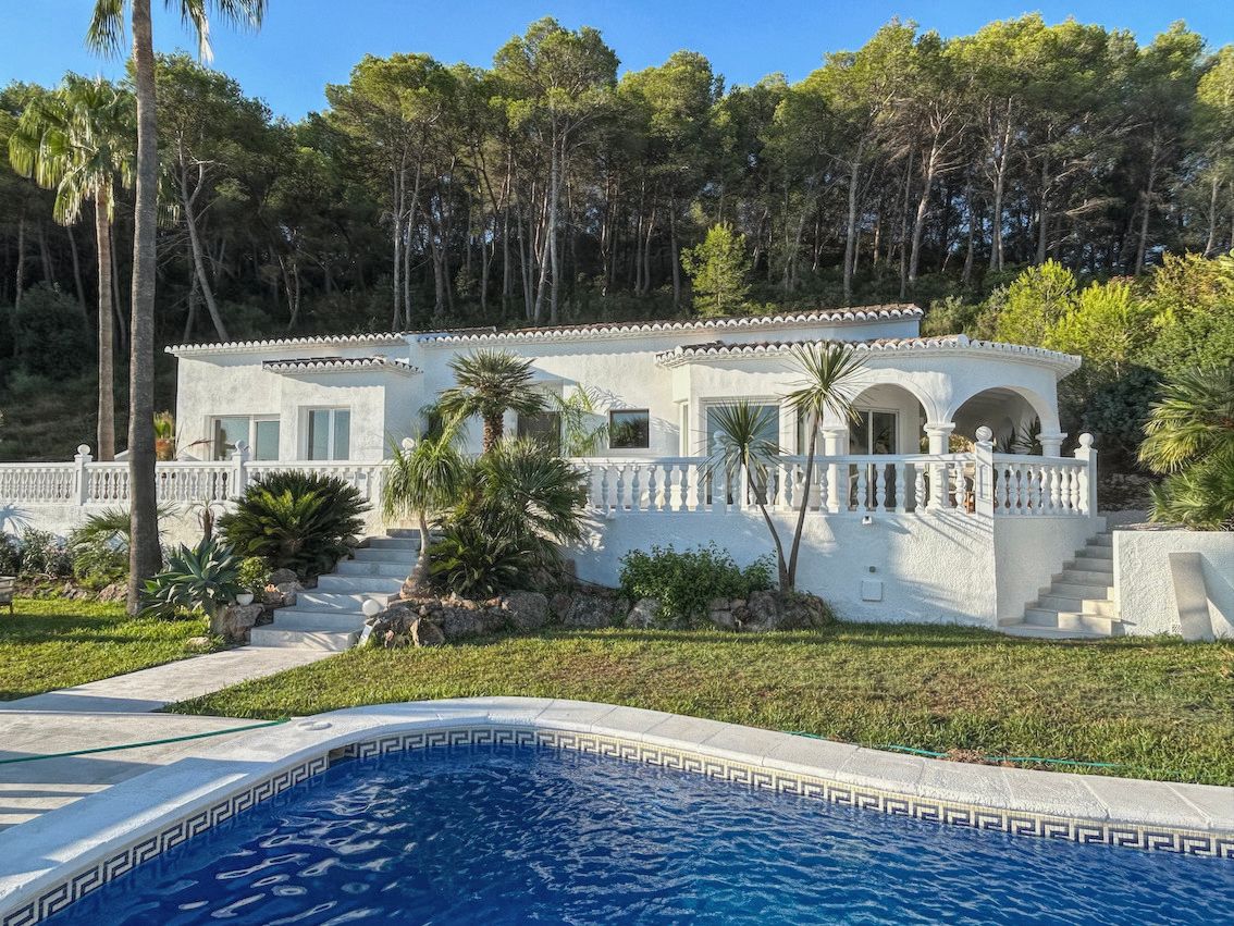Villa méditerranéenne blanche avec terrasse à balustrade, piscine ornée d'une frise grecque et vue sur la forêt de pins environnante.