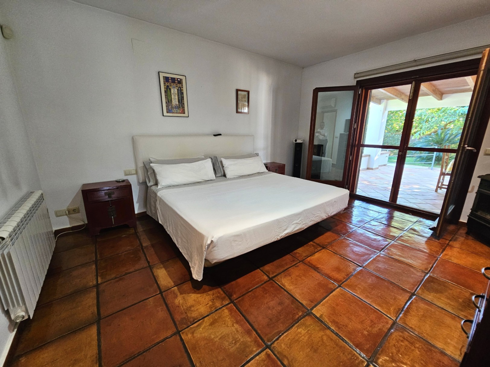 Chambre principale spacieuse avec sols en terre cuite artisanale et accès direct à la terrasse. Les baies vitrées sécurisées offrent une vue dégagée sur le jardin.