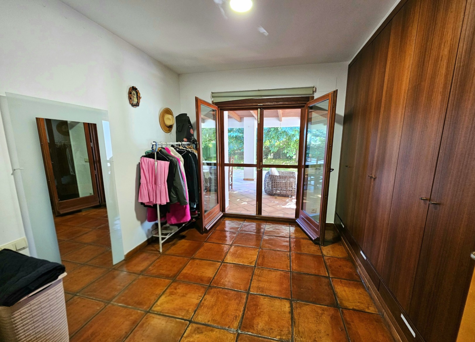 Dressing avec de grands placards intégrés en bois, sol en terre cuite artisanale et accès direct à la terrasse couverte par des portes vitrées.