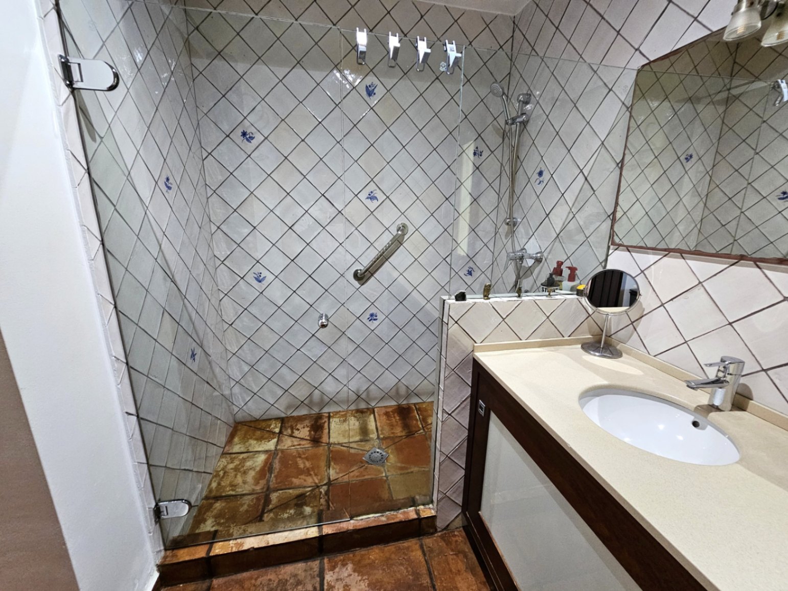 Salle de bain avec douche à l'italienne en verre et carreaux peints à la main. Elle dispose de sols en terre cuite artisanale et d'un meuble vasque avec plan de travail crème.