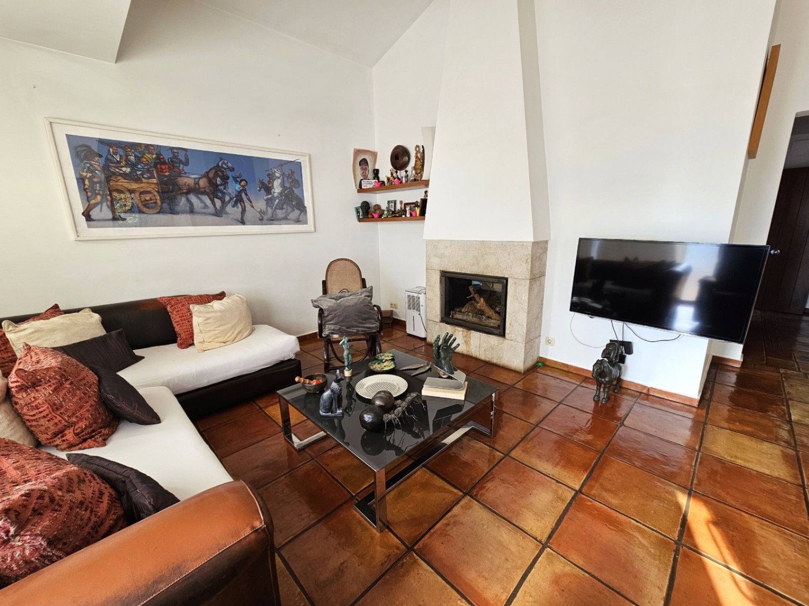 Salon avec sols en terre cuite artisanale et cheminée encastrée en pierre. L'espace offre de hauts plafonds, un mobilier moderne et une belle luminosité naturelle.
