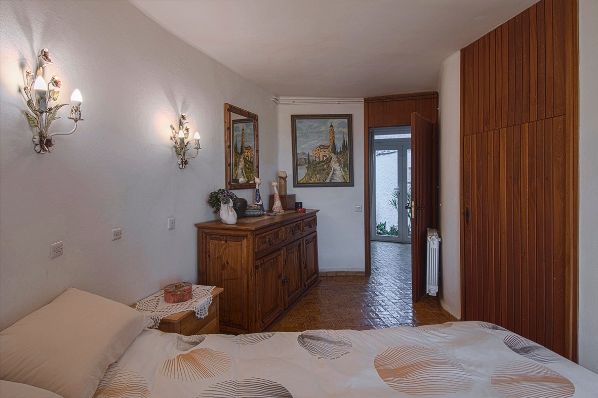 Chambre de style rustique avec sol en grès, armoire encastrée en bois et appliques décoratives. Elle dispose d'une commode en bois massif et d'un accès vers l'extérieur.