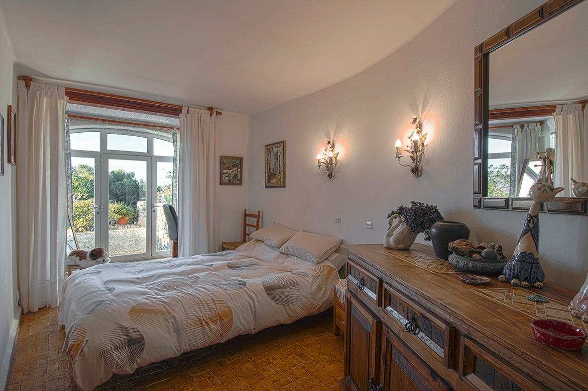 Chambre de style traditionnel avec sol en terre cuite, mobilier en bois rustique et porte vitrée cintrée offrant un accès direct vers l'extérieur.