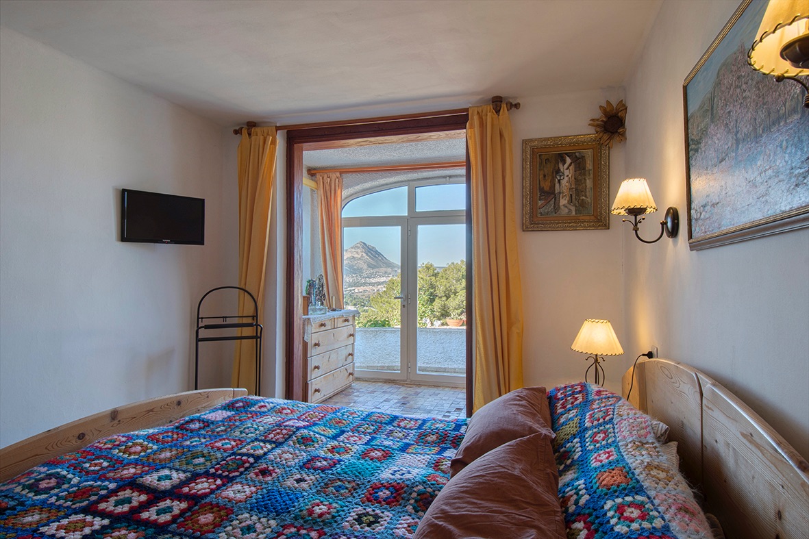 Chambre rustique avec mobilier en bois et accès direct à une terrasse privée offrant une vue dégagée sur les montagnes et la végétation.