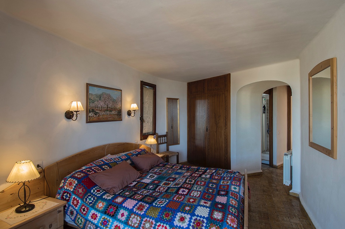 Chambre rustique avec placards intégrés en bois, sol en terre cuite et une arche élégante menant à la salle de bain attenante.