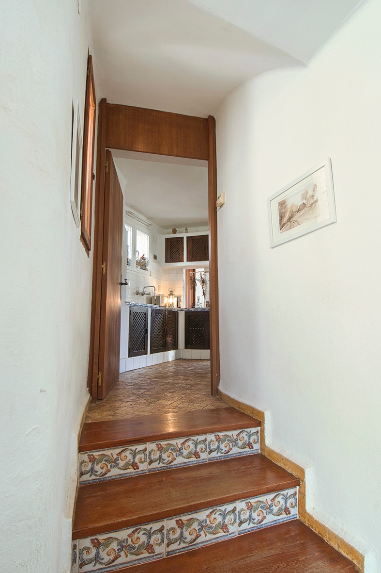 Escalier en bois aux contremarches carrelées menant à une cuisine rustique avec des meubles en bois sombre et des finitions traditionnelles.