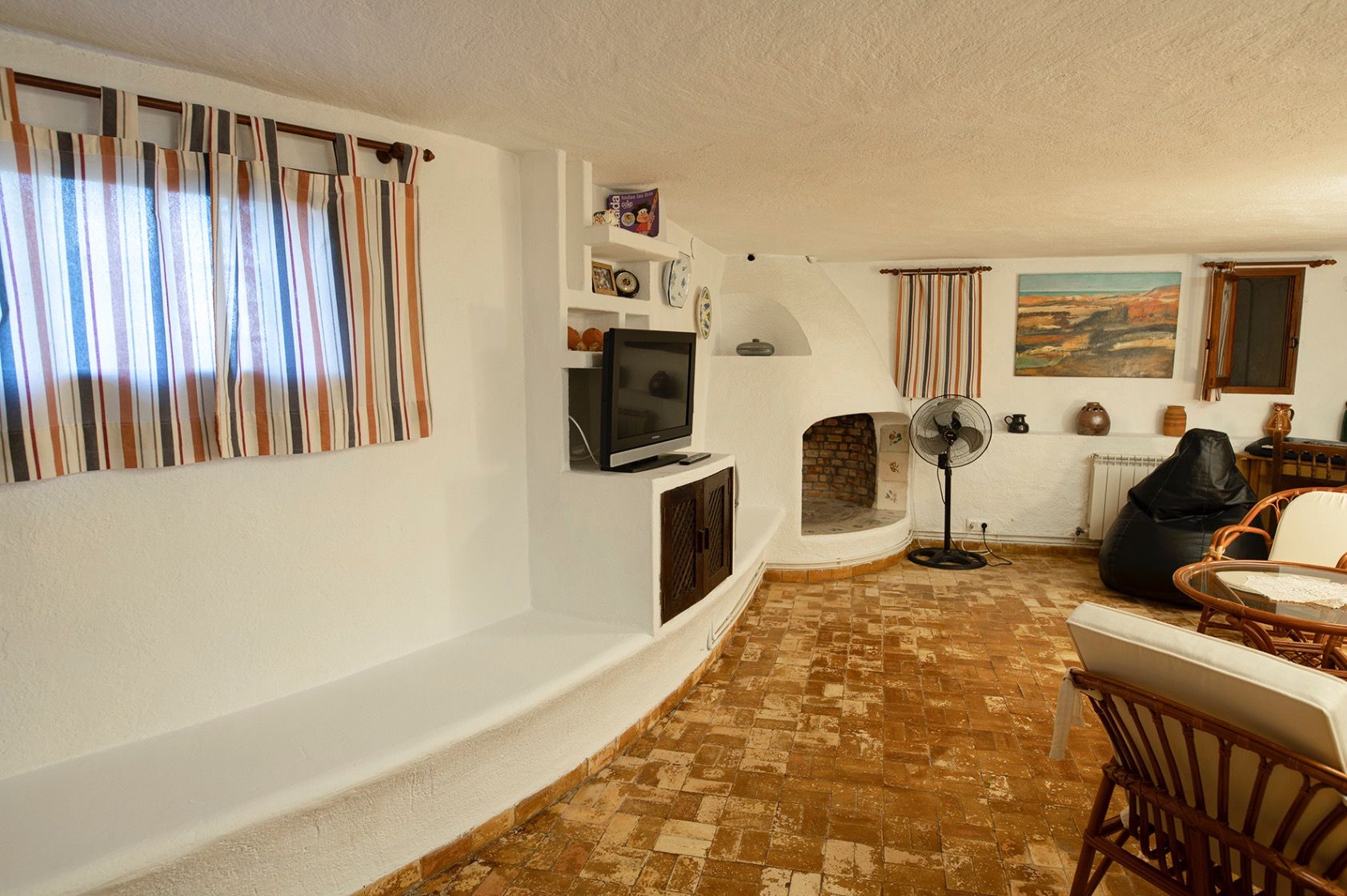 Espace de vie rustique avec cheminée intégrée, sol en terre cuite traditionnelle et étagères en maçonnerie blanche intégrées.