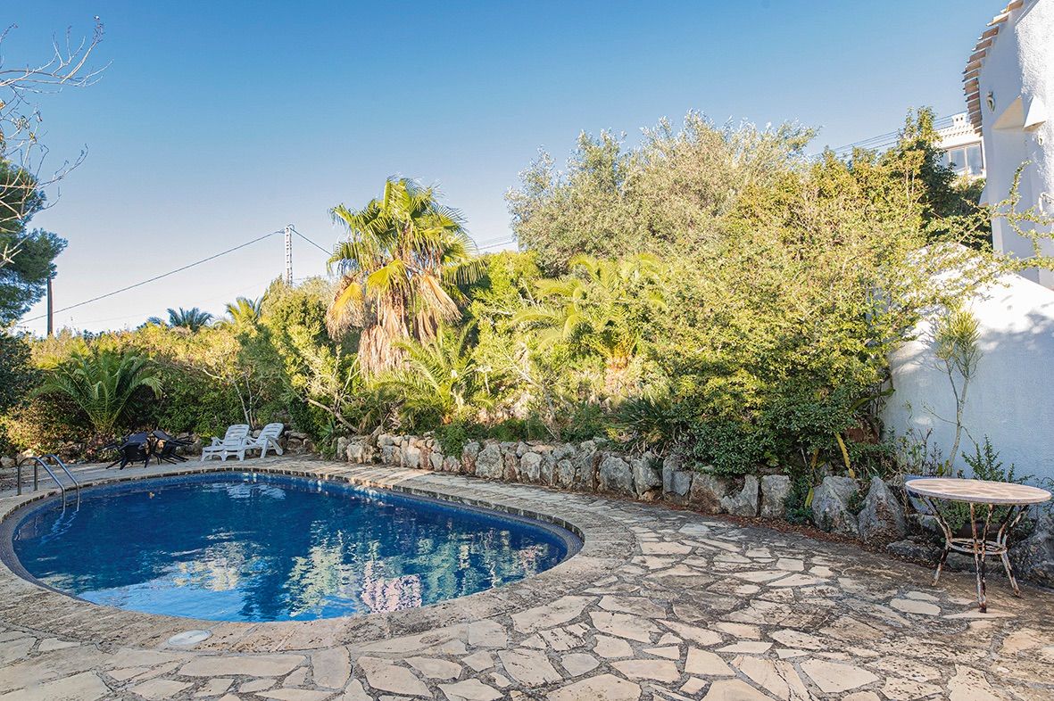 Piscine de forme libre entourée d'une terrasse en pierre naturelle et d'un jardin méditerranéen luxuriant. L'espace dispose de bains de soleil et de murets en pierre.