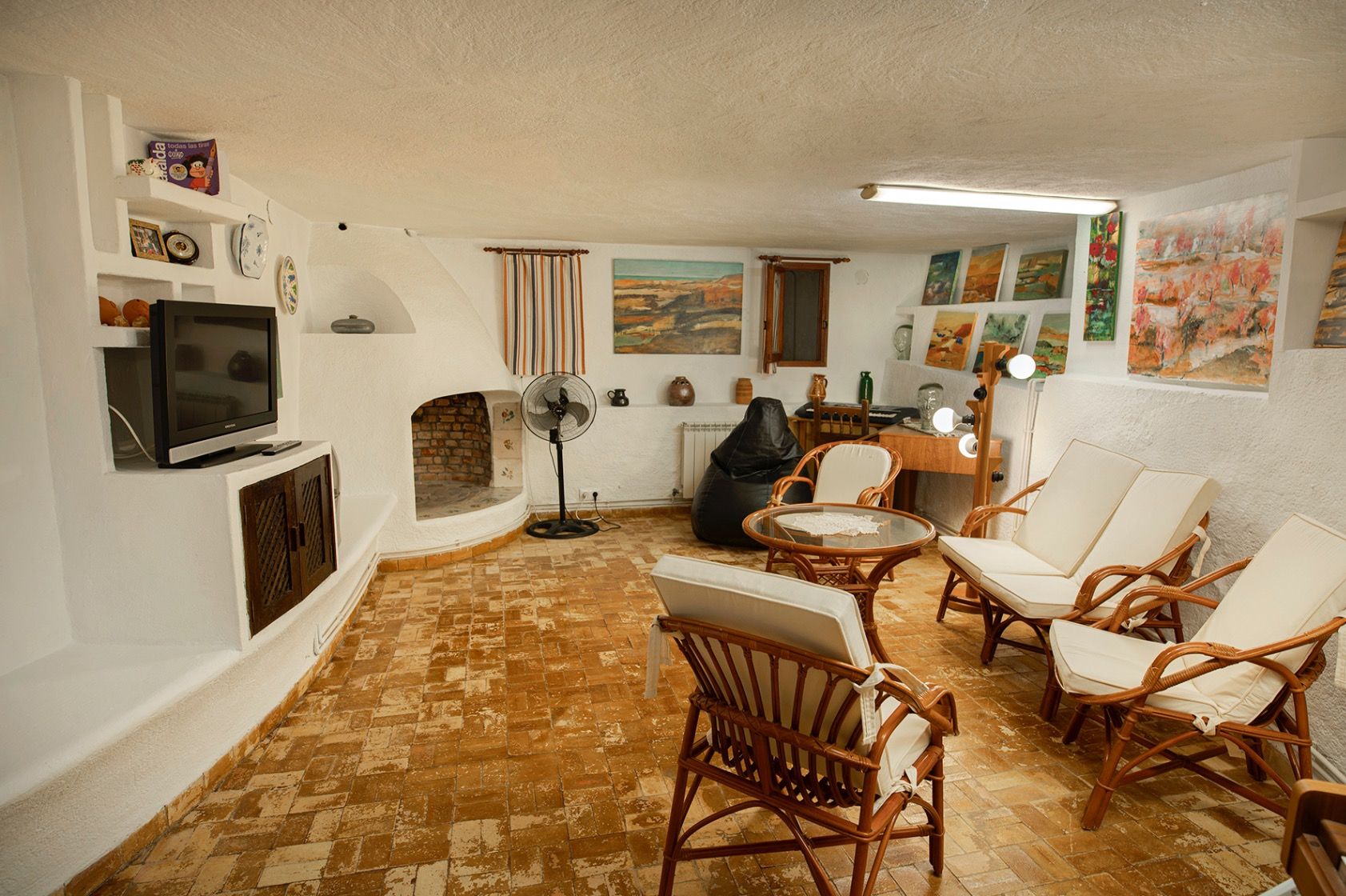 Salon rustique avec sol en terre cuite, cheminée intégrée et murs blanchis à la chaux. Comprend du mobilier en bambou et un coin atelier d'artiste.