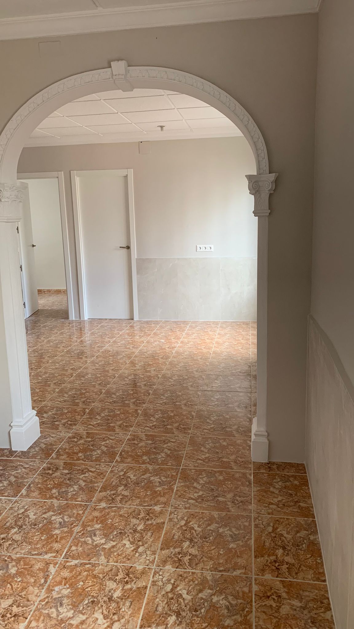 Couloir avec arche décorative classique, carrelage marbré aux tons terre de sienne et portes intérieures blanches menant aux différentes pièces de vie.
