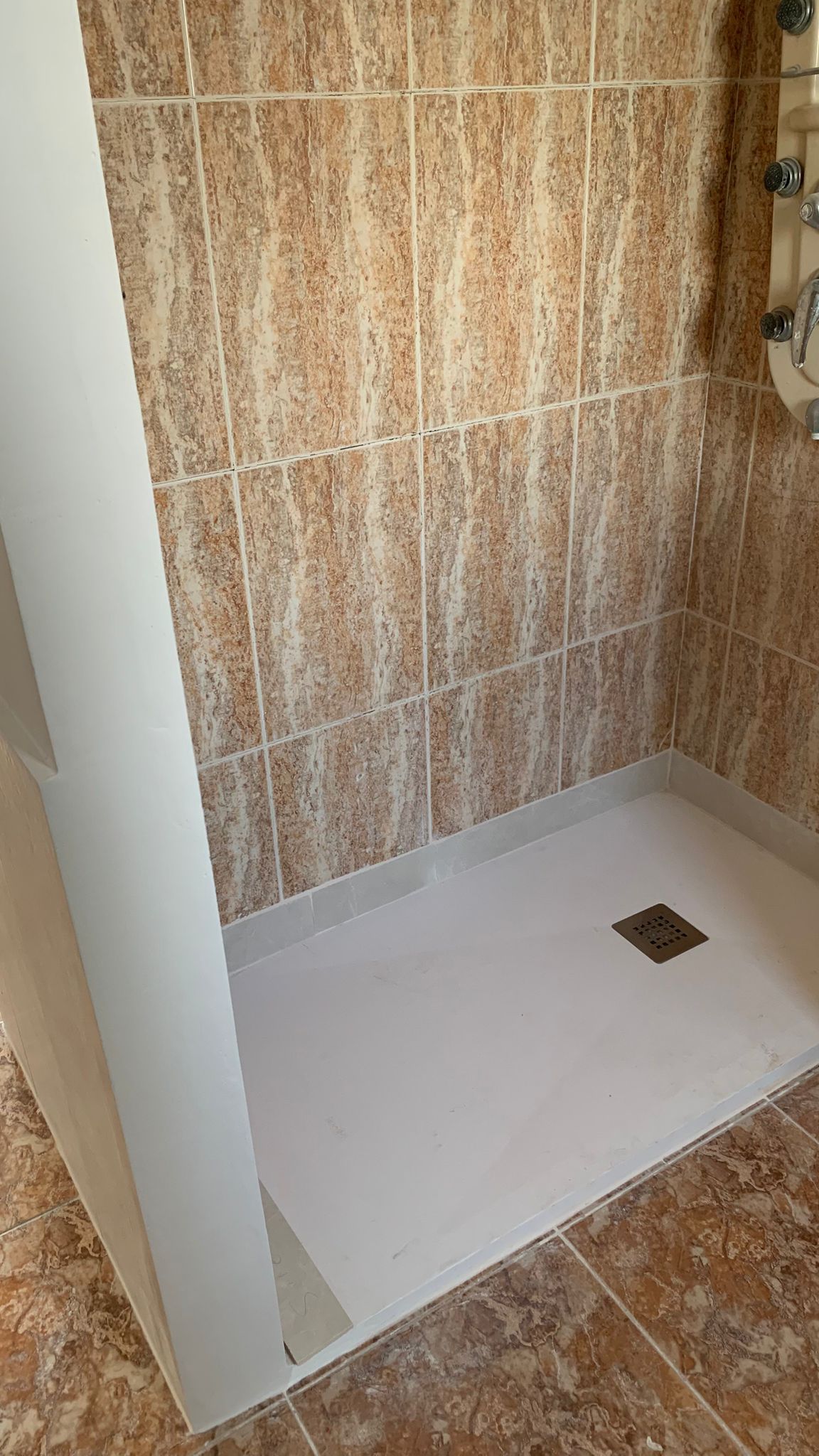 Douche à l'italienne avec receveur blanc, parois revêtues de carreaux effet marbre et colonne de douche avec buses d'hydromassage.