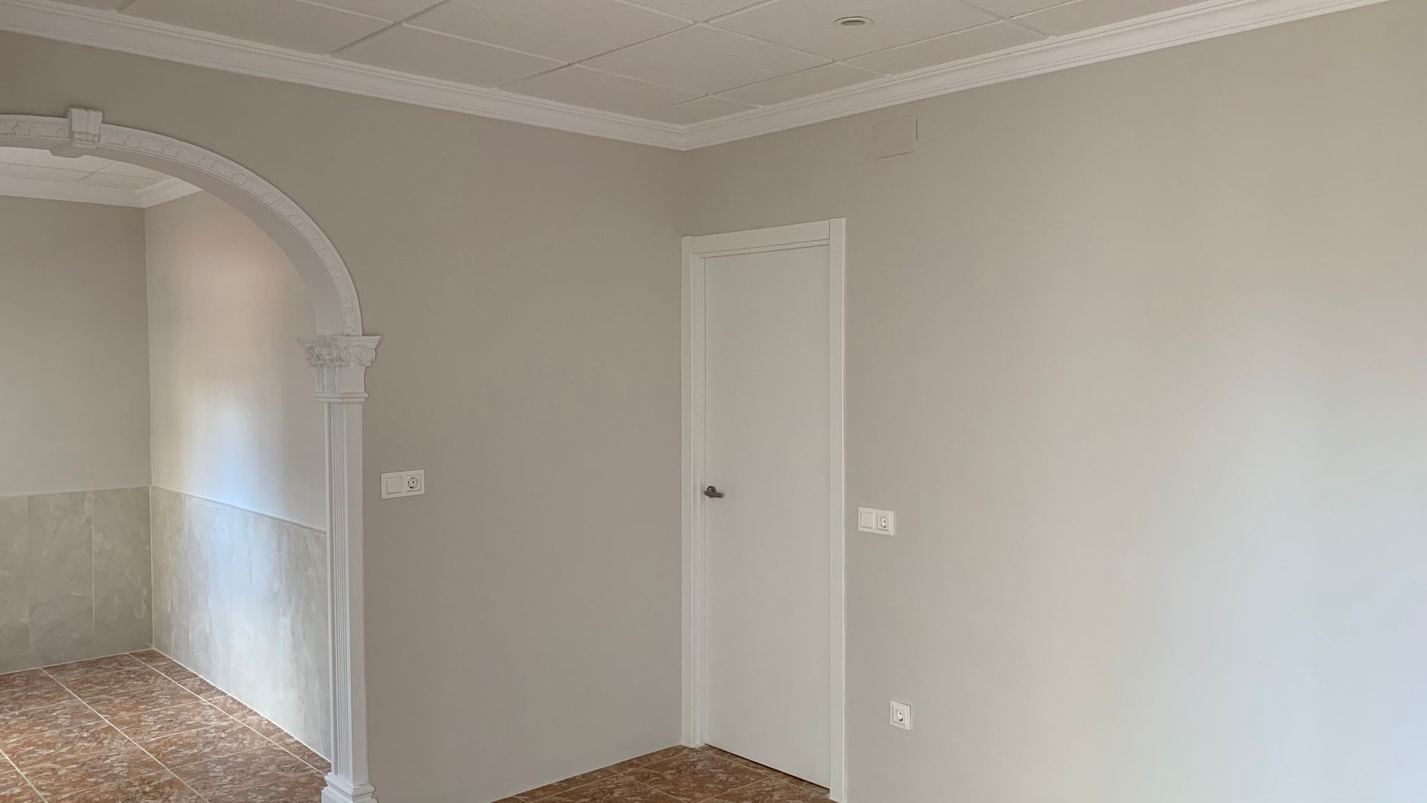Intérieur rénové présentant une arche décorative classique, des murs aux tons neutres, un sol en céramique et un plafond à caissons avec moulures élégantes.