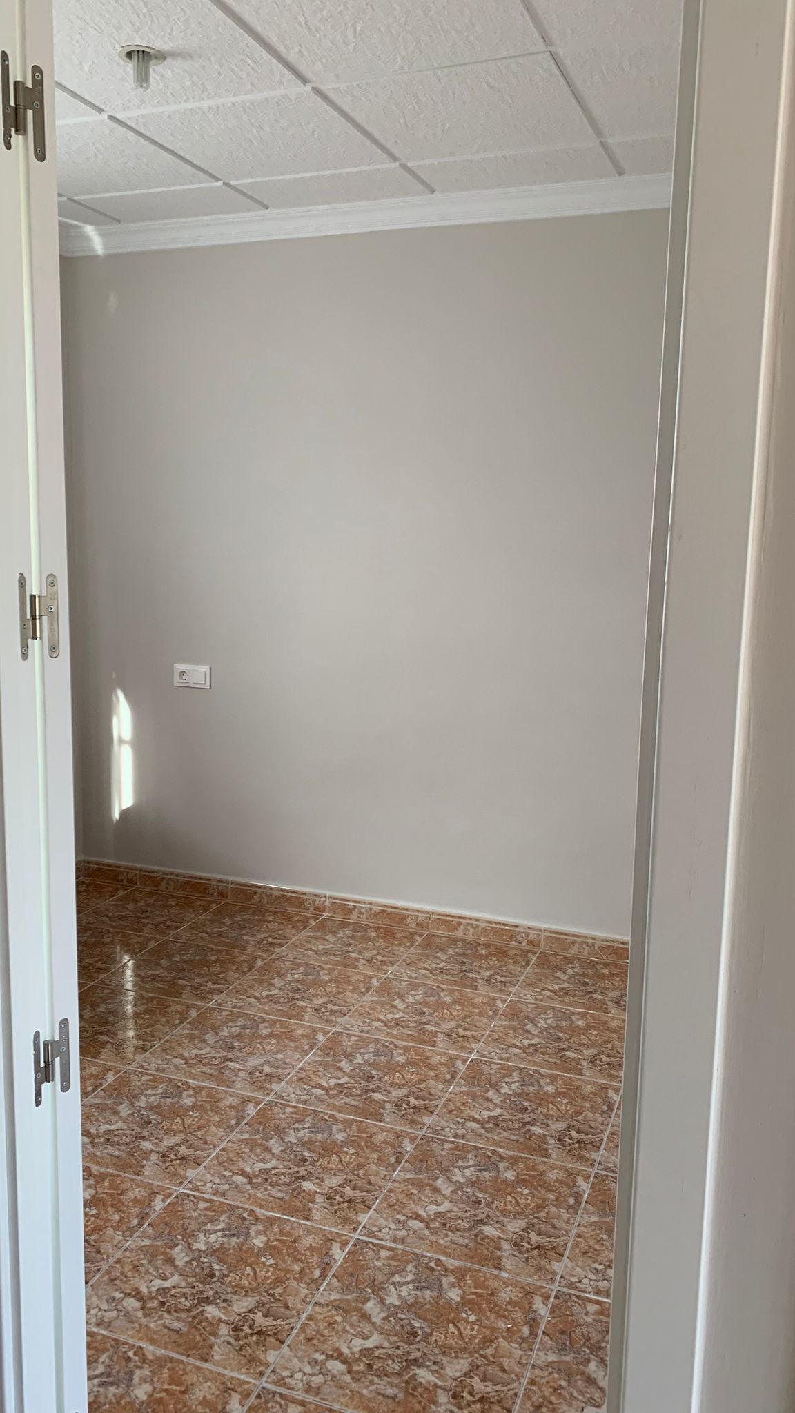 Pièce récemment rénovée avec un sol en grès cérame marbré aux tons bruns, des murs de couleur neutre et un plafond à panneaux texturés.