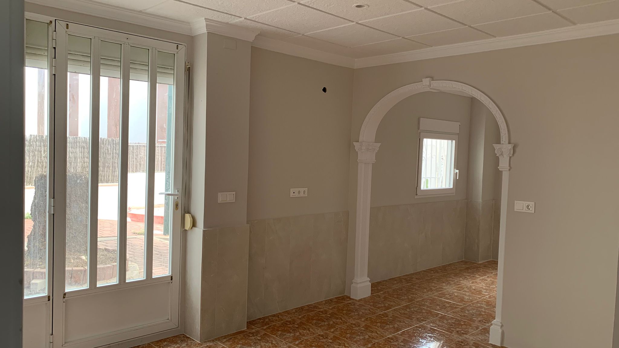 Salon avec arche décorative blanche, sol en grès et porte vitrée offrant un accès direct au patio extérieur de cet appartement rénové.