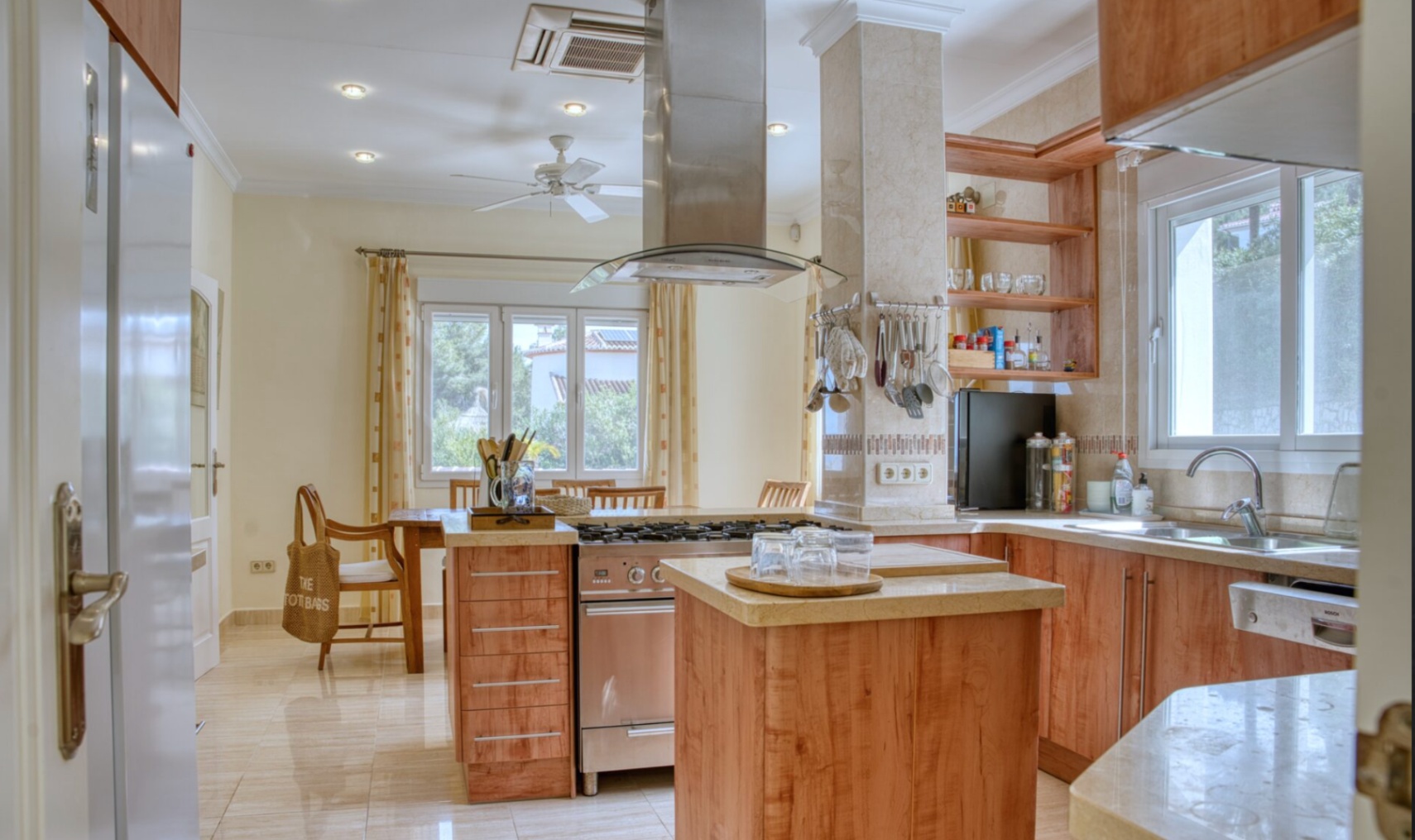 Cuisine équipée avec îlot central, plans de travail en pierre et électroménager en inox. Elle offre des rangements en bois, une hotte design et un coin repas attenant.