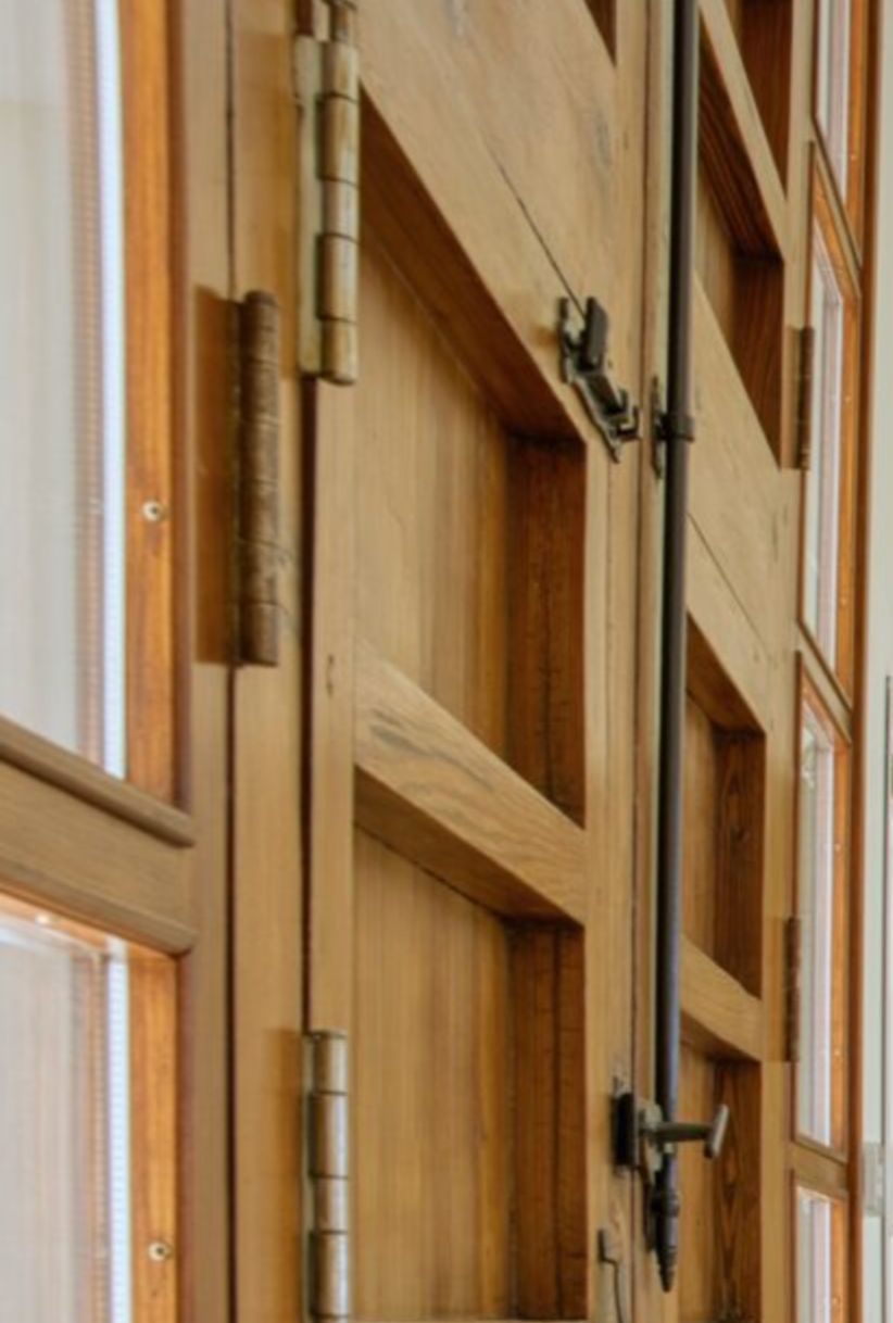Détail de menuiserie en bois massif avec charnières métalliques traditionnelles et système de fermeture à crémone, illustrant le soin apporté aux finitions.