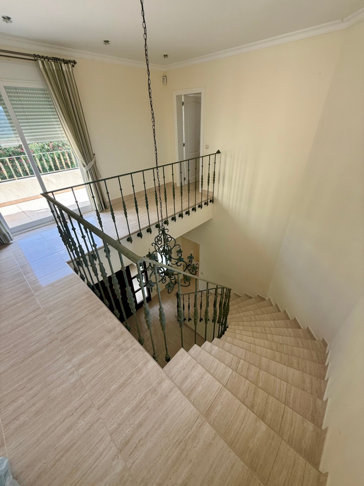 Escalier courbe en pierre naturelle avec rampe en fer forgé, menant à un palier supérieur lumineux offrant un accès direct au balcon.