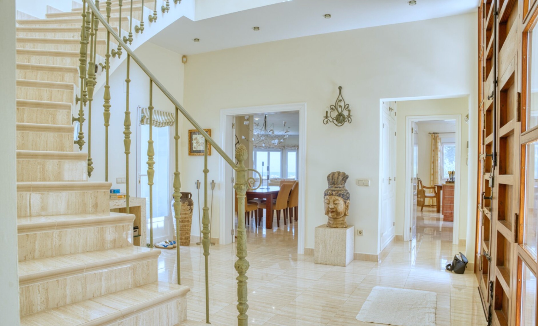 Hall d'entrée avec escalier en marbre travertin et rampe en fer forgé. Les sols en pierre polie mènent à une salle à manger lumineuse avec vue sur la Méditerranée.