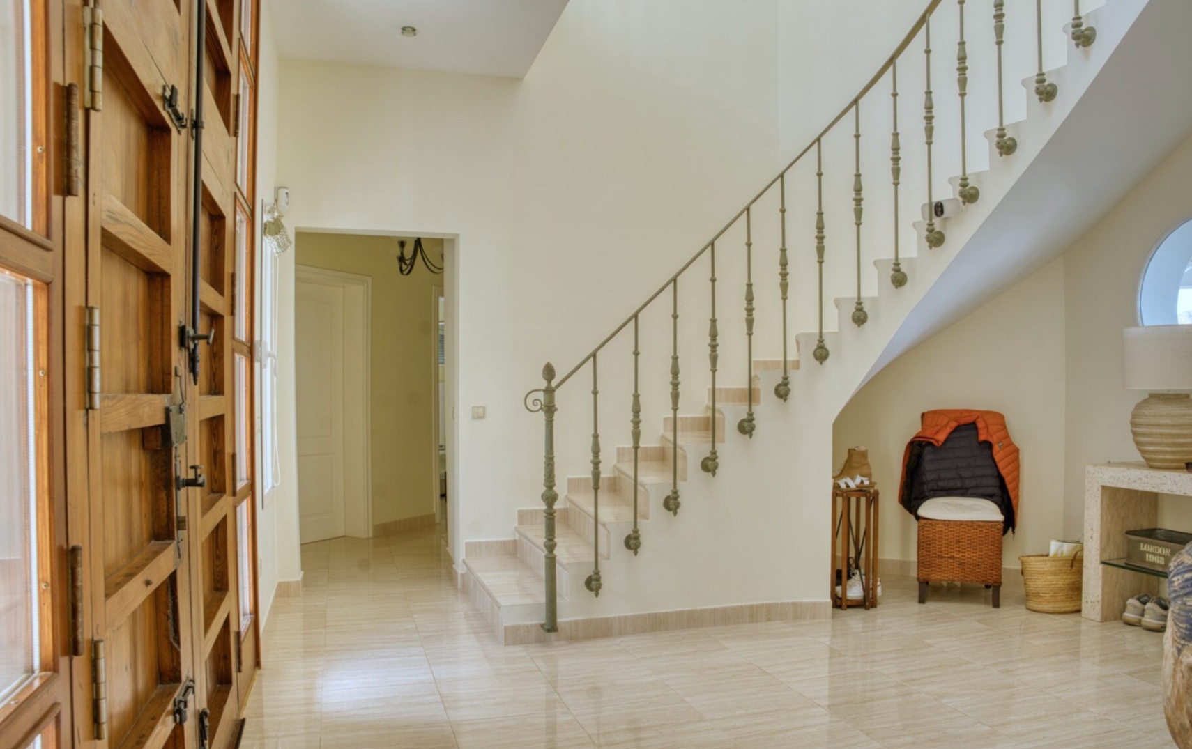 Hall d'entrée avec porte en bois massif, sol en marbre poli et un escalier courbe doté d'une rampe en fer forgé ornementale.