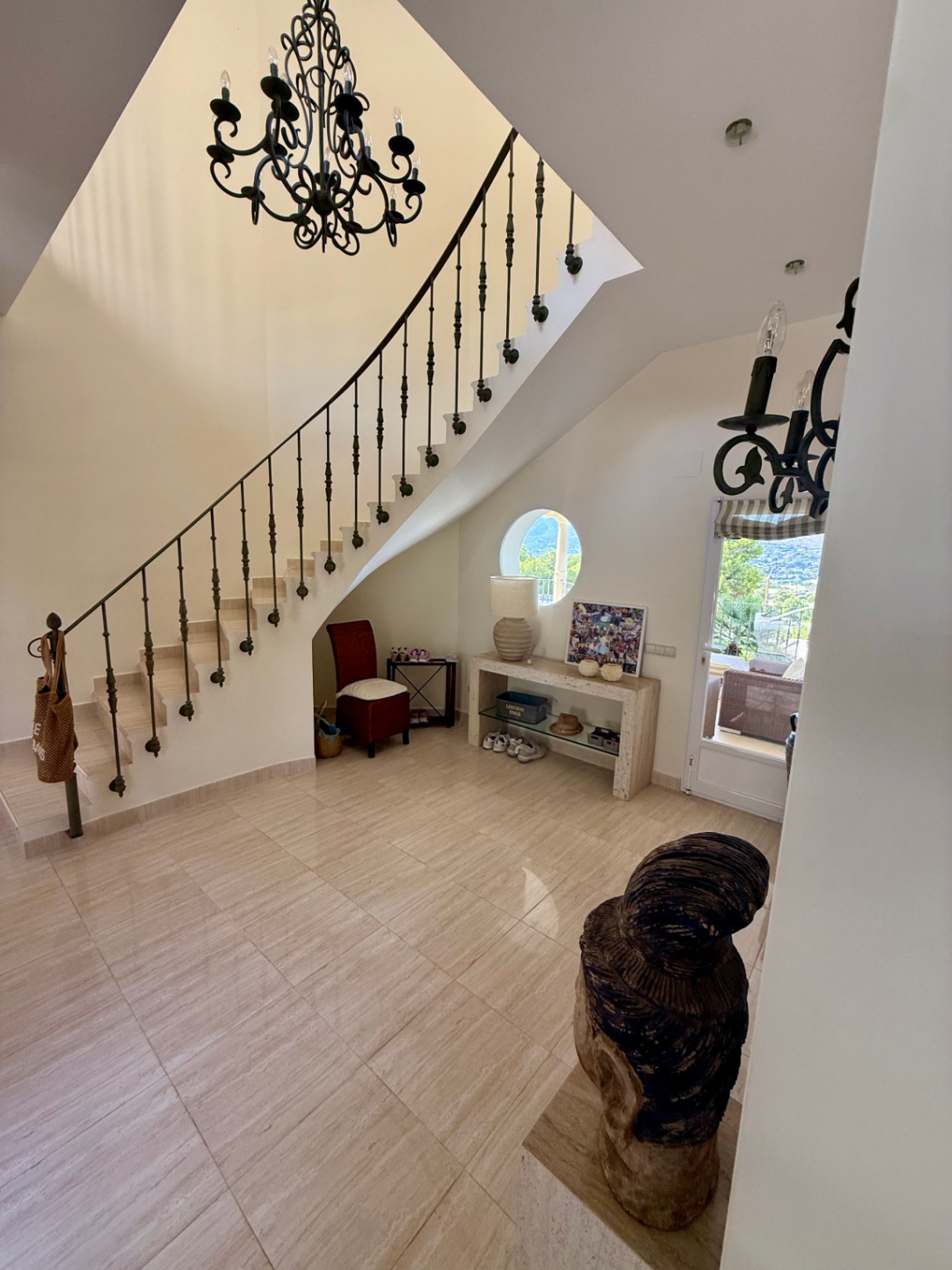 Hall d'entrée avec sol en marbre, escalier en fer forgé et une fenêtre circulaire offrant une vue dégagée, complété par un lustre classique.