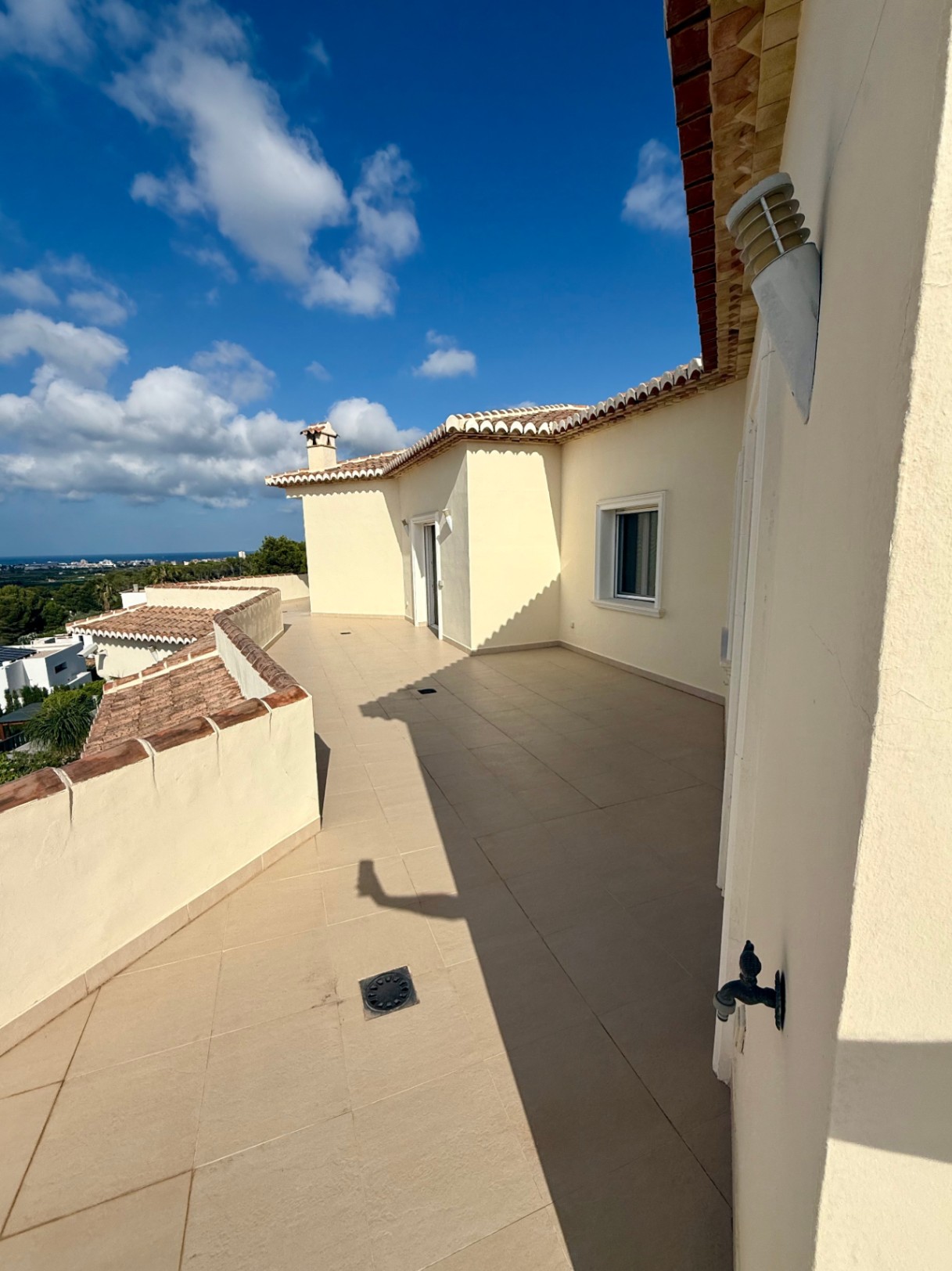 Vaste terrasse à l'étage supérieur avec carrelage beige et vue panoramique sur la mer. L'architecture courbe est soulignée par des finitions en tuiles traditionnelles.