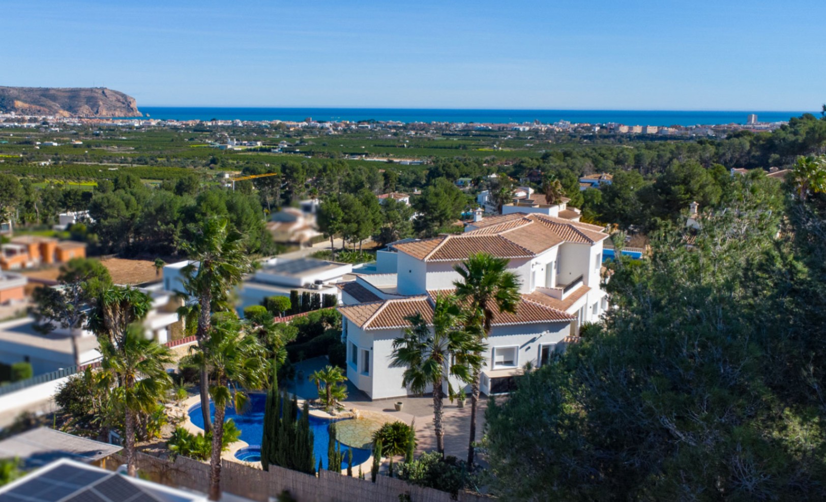 Vue aérienne de la villa aux toits de tuiles, piscine de forme libre et panorama dégagé sur la mer Méditerranée et le littoral de Jávea.