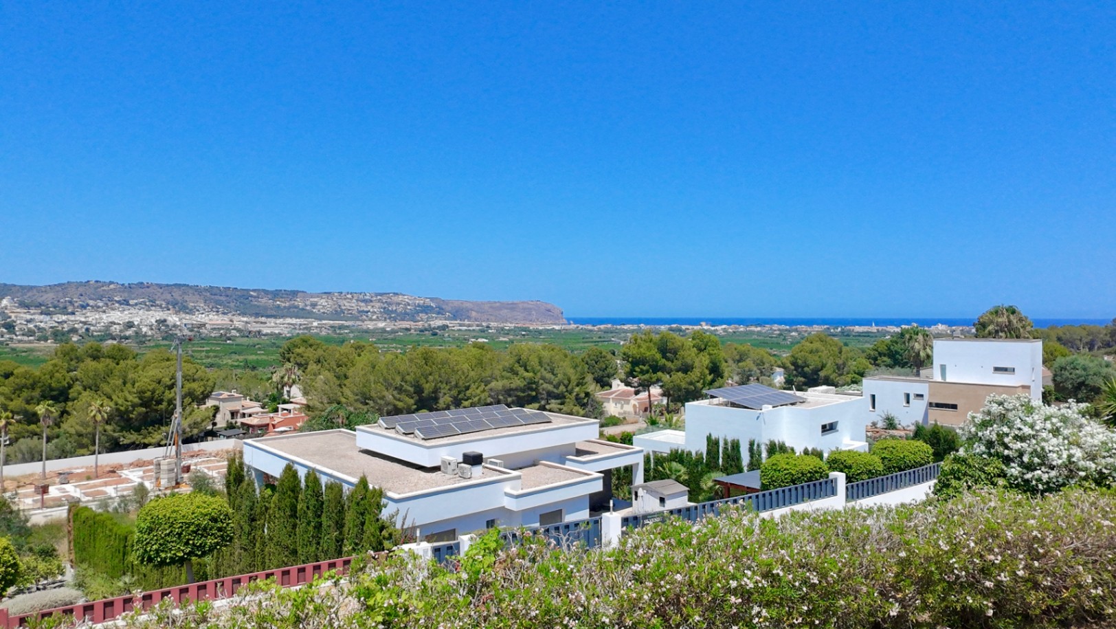Vue panoramique surélevée sur la mer Méditerranée et la vallée, illustrant l'architecture moderne des villas environnantes avec panneaux solaires et jardins arborés.